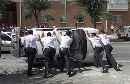 Agentes de policía voltean el coche camuflado que fue volcado por vecinos del barrio del Parque Amate tras el tiroteo.