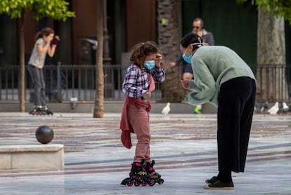 Una niña en patines y con mascarilla conversa con una mujer esta tarde en la Plaza Nueva de Sevilla.