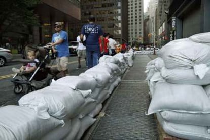 Unos peatones andan al lado de los sacos terreros puestos para proteger una calle de Manhattan, ante el riesgo de inundación.