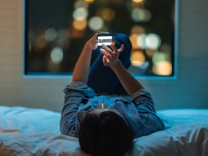 Chica tumbada en la cama boca arriba con el móvil de noche.