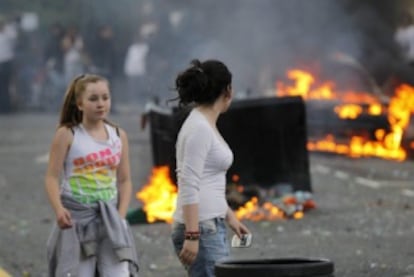 Dos chicas observan cómo un grupo de jóvenes queman un coche y contenedores de basura en Hackney, al este de Londres.