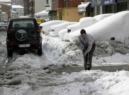 Un hombre despeja con una pala el acceso a la calle principal de la localidad de Guardo donde los coches aparecen sepultados por la nieve debido al temporal de frío y nieve.