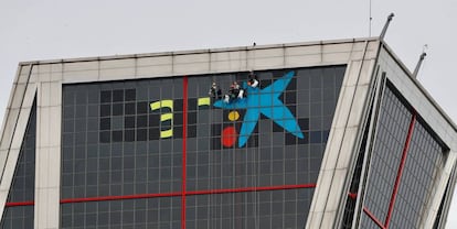 Un grupo de operarios cambia esta mañana de sábado el logotipo de Bankia por el de CaixaBank en una de las torres Kio de Madrid, sede central de Bankia en la capital.