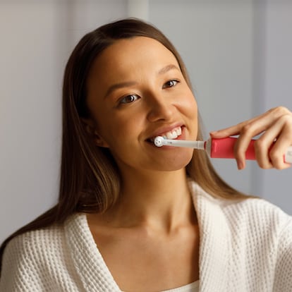Una chica cepillándose los dientes con un cepillo eléctrico.