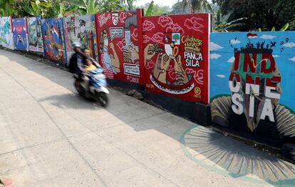 Dos personas que viajan en moto pasan cerca de un mural hecho por artistas para concienciar sobre el peligro del coronavirus, en Bogor (Indonesia).