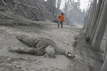 El cuerpo de una víctima de la erupción del volcán Merapi (Indonesia), permanece sobre la carretera cubierto de cenizas volcánicas mientras un hombre acude a su rescate.