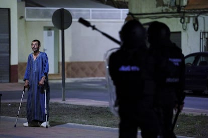 Un migrante con muletas permanece cerca de agentes de policía, en medio de disturbios en Torre Pacheco, este domingo.