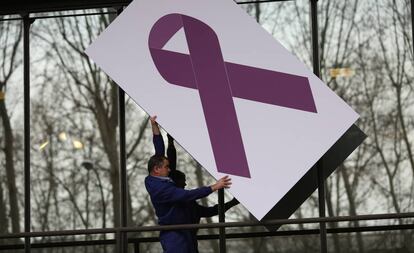 Un operario coloca un panel con una lazo gigante morado en contra de la violencia de género en la fachada del Ministerio de Sanidad.