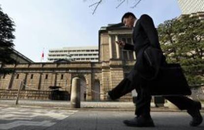 Un viandante mira su teléfono móvil mientras pasa delante de la sede del Banco de Japón (BOJ), Masaaki Shirakawa, en Tokio (Japón). EFE/Archivo