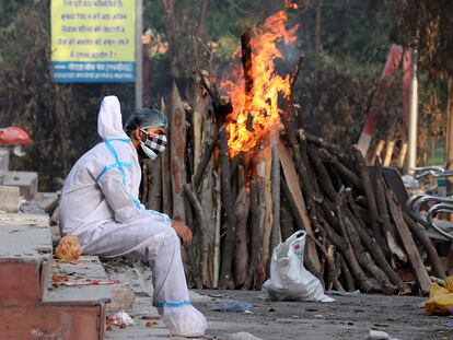 Un hombre ataviado con un traje aislante permanece sentado tras realizar rituales funerarios a sus familiares difuntos, el lunes en Nueva Delhi.