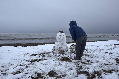 Un niño juega con un muñeco de nieve en la playa de Les Marines, en Denia, completamente nevada desde primeras horas de la mañana.