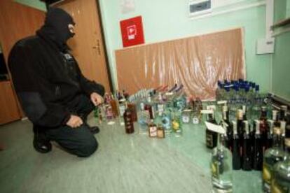 Un policía de aduanas se arrodilla junto a 200 botellas confiscadas de alcohol ilegal encontradas en dos apartamentos en Kielce (Polonia). EFE/Archivo