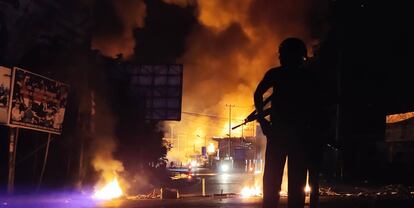 Un policía indonesio permanece en guardia junto a un edificio en llamas.