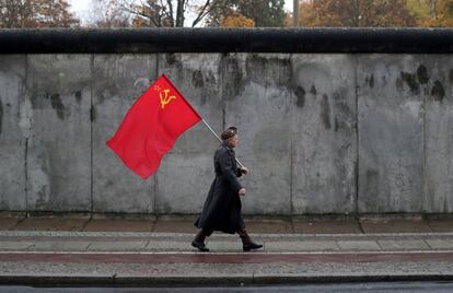 Um homem, vestido com uniforme e com uma bandeira soviética, protesta contra a ditadura do capitalismo em frente a uma parte do Muro de Berlim, no sábado.