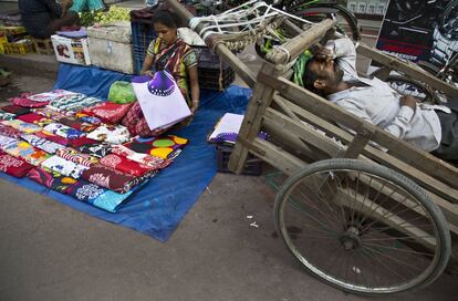 Uma mulher indiana prepara a roupa que vai vender em seu posto de rua enquanto um homem dorme em uma carroça a seu lado em um mercado de Gauhati (Índia), no dia 7 de março.