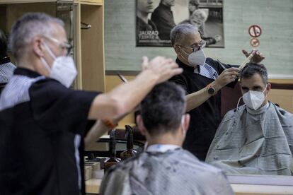 Angel Mancebo atiende a su primer cliente en su peluquería del barrio de Poble Sec de Barcelona tras su reapertura, este lunes.