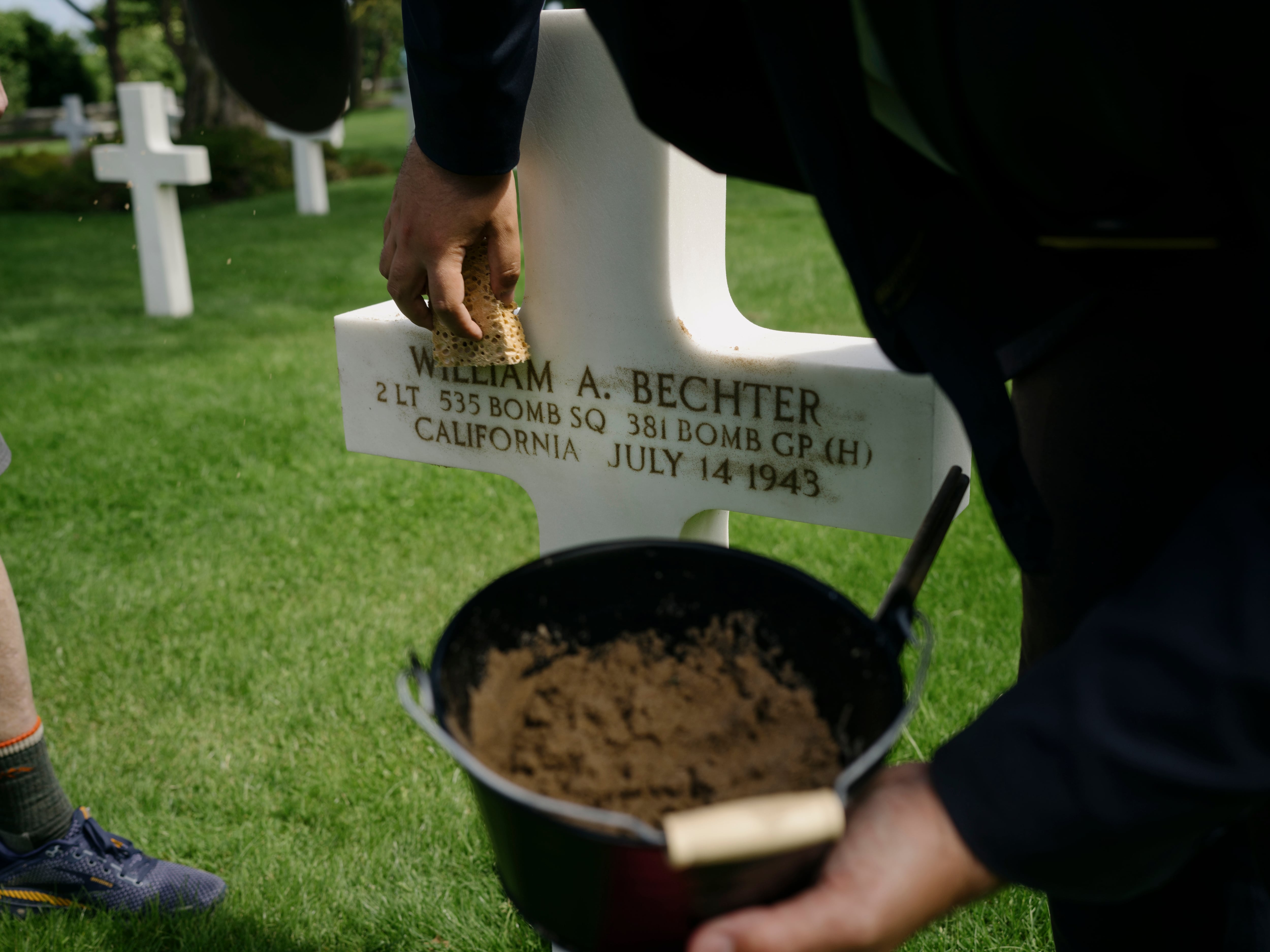 La familia Burridge pone arena de la playa para resaltar la inscripción de la tumba de William A. Bechter, un amigo de la familia, en el cementerio Americano en el pueblo de Colleville-sur-mer.