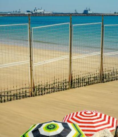 Parte de la playa acotada por seguridad. Al fondo, varios barcos de la Marina española.