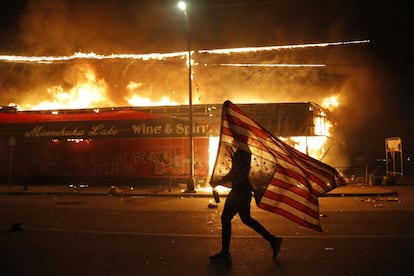 Un manifestante sujeta una bandera de Estados Unidos durante los disturbios en Minneapolis, esta madrugada. La tercera noche de protestas para reclamar justicia por la muerte de George Floyd, un afroamericano muerto bajo custodia policial el pasado lunes, ha vuelto a estar marcada por la violencia.