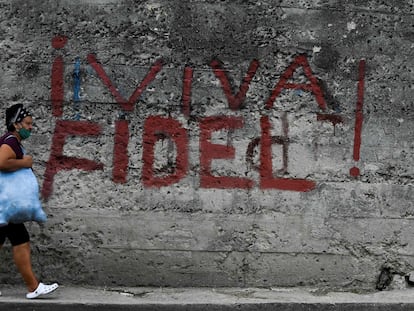 Una mujer camina delante de una pintada en la que se lee ¡Viva Fidel!