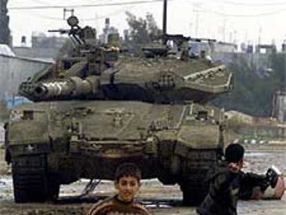 Dos palestinos descalzos lanzan piedras contra un tanque israelí.