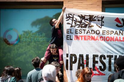 Tres jóvenes fijan un cartel a la fachada de La casa del estudiante, de la Universidad Complutense de Madrid, frente al campamento pro palestino.