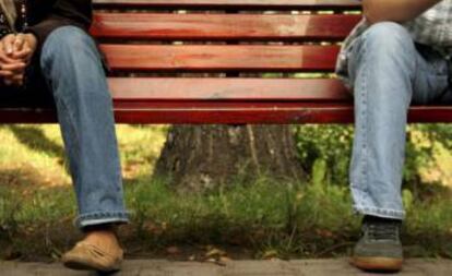 Un hombre y una mujer, sentados de forma separada en un banco.