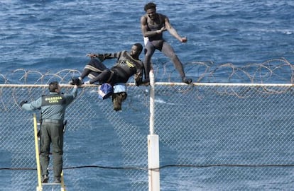 Dos inmigrantes intentan saltar la valla de Ceuta frente a un guardia civil. 