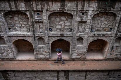 Un hombre indio se cubre de la lluvia mientras camina dentro del Agrasen ki Baoli, en Nueva Delhi (India).