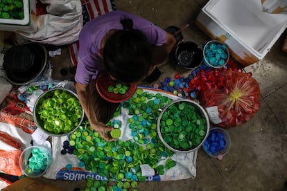 Un empleado clasifica tapas de plástico por colores en el centro de recogida y reciclaje de Precious Plastic en Bangkok. Sus máquinas trituran, funden y moldean los residuos transformándolos en cuencos, vasos y muebles. La población local vende estos objetos a Precious Plastic y utiliza los beneficios para mantener a sus familias.