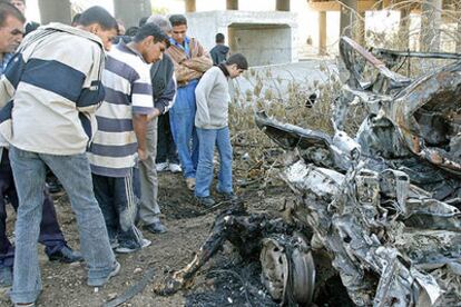 Varios iraquíes observan el cadáver quemado de un suicida bajo los restos de un coche bomba.