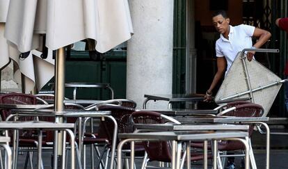 Un trabajador coloca mesas de una terraza. 