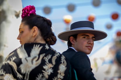 Un hombre corto y una mujer vestida de flamenca montados en un caballo en una de las paradas de la Feria.