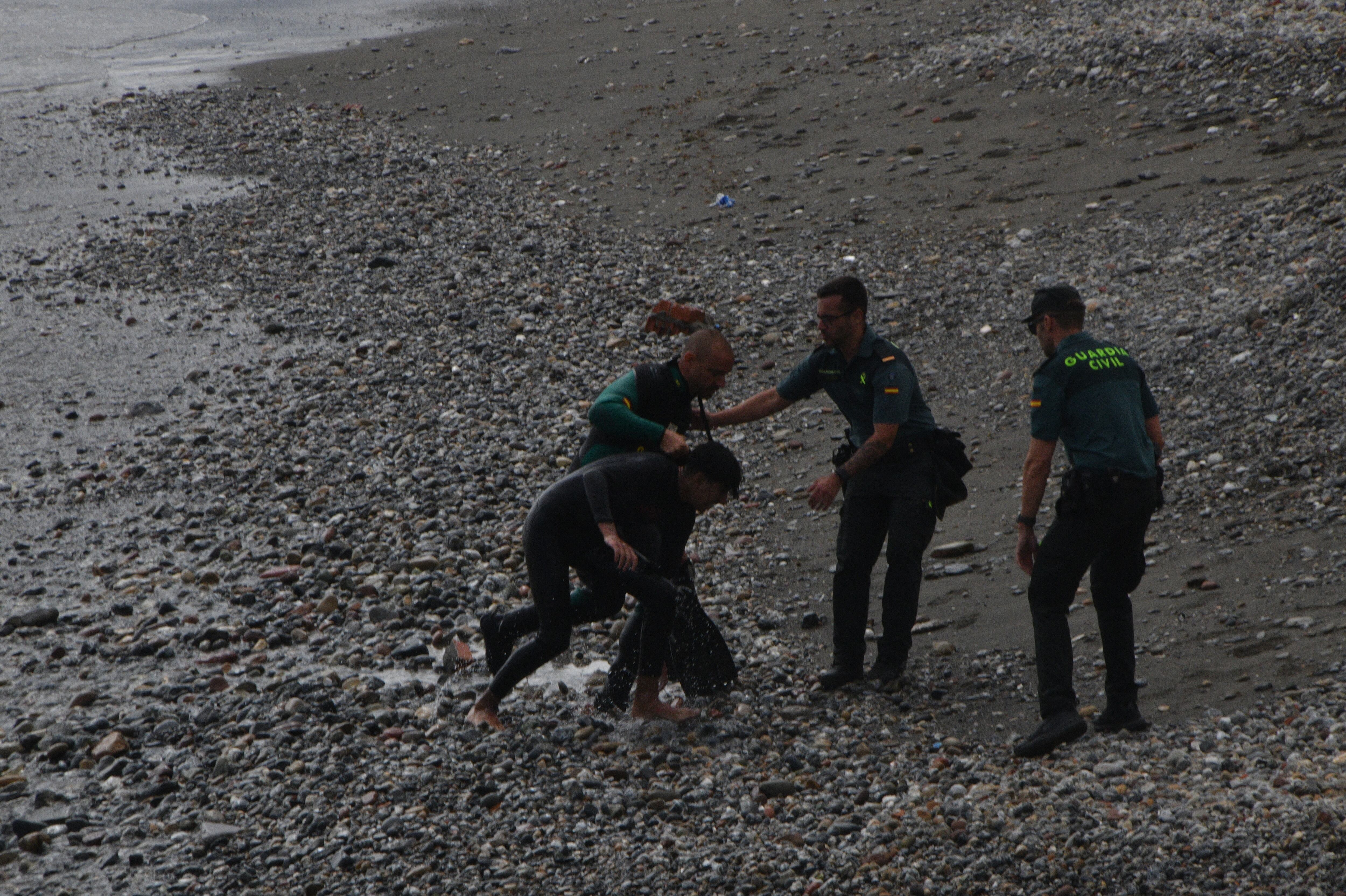 Tres agentes reciben a un joven recién salido del mar, en Ceuta, este sábado.
