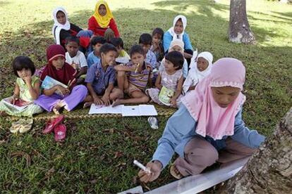 Un grupo de niños asiste a clase bajo los cocoteros en un campo de desplazados de Ladong, en la región indonesia de Aceh.