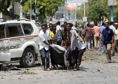 Varios civiles cargan con el cadáver de un hombre muerto en una explosión cercana a un hotel, en Mogadishu (Somalia).