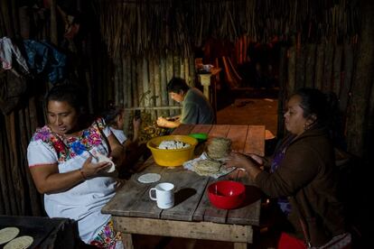 Fermina prepara comida para la festividad maya del Biix. Su hija ilumina con la linterna del teléfono al marido, para que termine de pintar una talla de madera que venderá al día siguiente en Mérida.