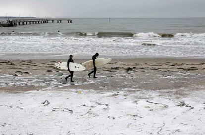 Dos surfistas caminan por una playa nevada del Mar Báltico, cerca de Luebeck, Alemania.