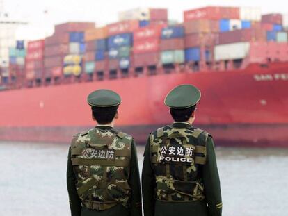 Dos polic&iacute;as esperan la llegada de un buque de carga en el puerto de Qingdao, China.