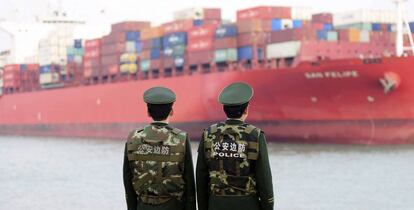 Dos polic&iacute;as esperan la llegada de un buque de carga en el puerto de Qingdao, China.