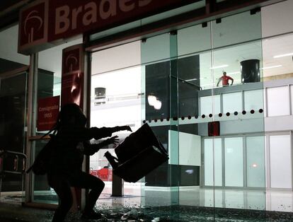 Un manifestante lanza una silla en la entrada de un banco en el centro de São Paulo (Brasil).