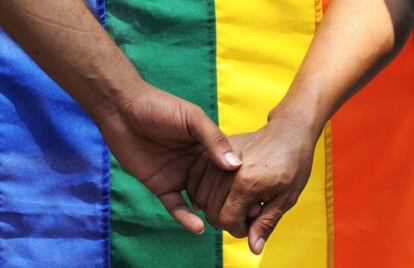 Dos hombres de la mano ante una bandera gay. 