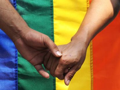 Dos hombres de la mano ante una bandera gay. 