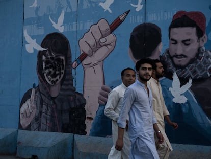 Tres afganos pasan delante de un mural en el centro de Kabul en el que han pintado de negro la cara de una mujer que representa a las afganas votando.