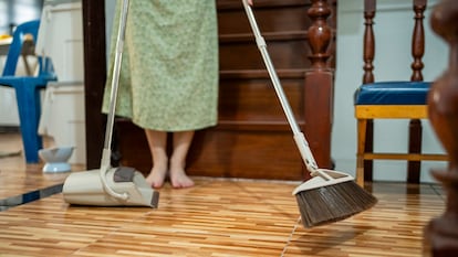 Los pies de una mujer se ven junto a una escoba y un recogedor, mientras estos están en uso