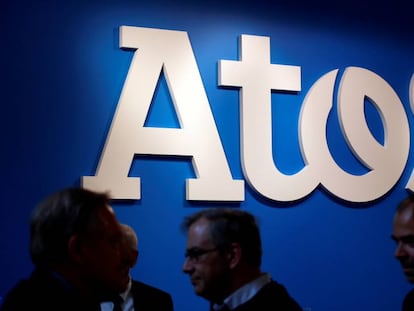 Varias personas pasan junto a un logo de Atos durante un evento sobre supercomputaci&oacute;n en Par&iacute;s. 