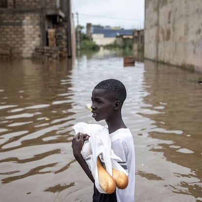 A young boy carries baguettes through the flooded neighbourhood of Keur Massar, Dakar, on August 20, 2021. - Each year the neighbourhood of Keur Massar deals with heavy flooding during the peak of the rainy season. Families living in Keur Massar pack up their belongings and move out of the area during this period. Last year, after the worst flooding to date, the government gave over fifteen million West African Francs towards a project to help fight the flooding and displacement in this area. (Photo by JOHN WESSELS / AFP)