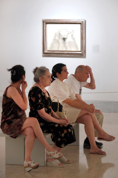 La familia del pintor Antonio López observa uno de los cuadros desde un banco.