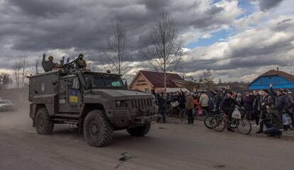 Soldados ucranios saludan desde un vehículo militar a los residentes locales que esperan en una cola para recibir ayuda humanitaria, en la ciudad de Trostianets (noreste), este miércoles.