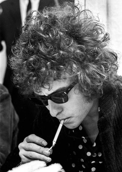 Dylan durante una conferencia de prensa en Suecia (1966). Convertido al rock, y siendo parte de la Generación Beat, su imagen evoluciona dejándose crecer el cabello –que rizado y revuelto le da un aire sexy–; utiliza las Way Farer, de Ray Ban y comienza a vestirse de riguroso negro con camisas estampadas que se erigen como icono rockero. Mención especial a la longitiud de las uñas de la mano derecha con la que se enciende el cigarrillo.